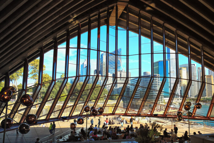 A view from inside Bennelong restaurant overlooking Circular Quay cityscape and the motion of the buzzing Sydney Opera House restaurant. Bennelong Bar review by White Caviar Life.
